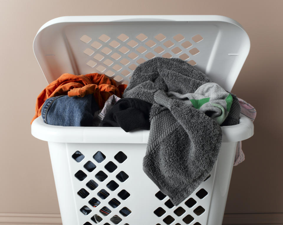 Laundry basket filled with various clothes and towels, placed against a plain background