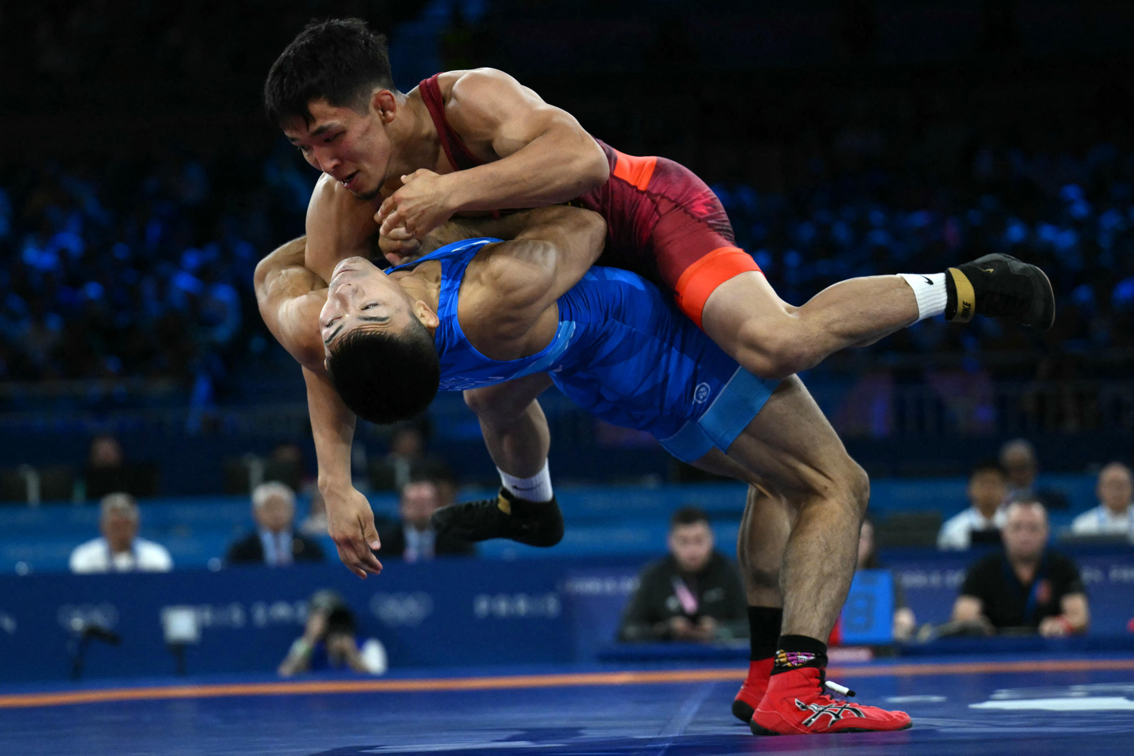 Kyrgyzstan's Zholaman Sharshenbekov (red) wrestles Japan's Kenichiro Fumita (blue) in their men's greco-roman 60kg wrestling semi-final match at the Champ-de-Mars Arena during the Paris 2024 Olympic Games, in Paris on August 5, 2024. (Photo by Luis ROBAYO / AFP)