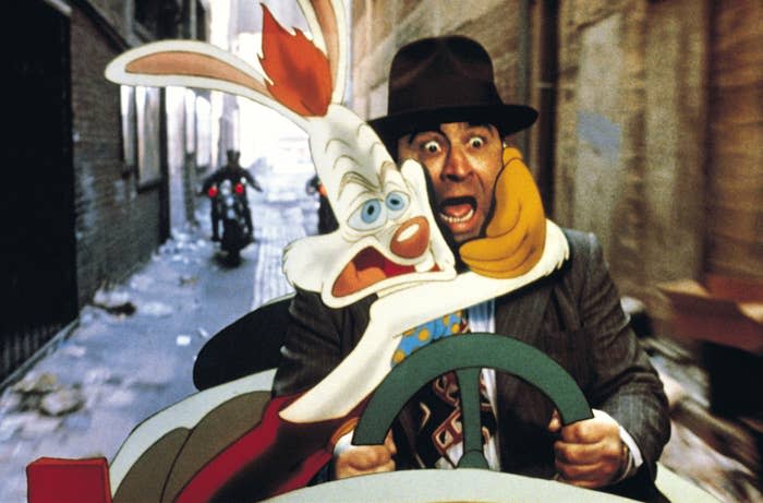 Bob Hoskins drives a car looking shocked with Roger Rabbit in his lap. Both appear scared as they navigate through a narrow alleyway