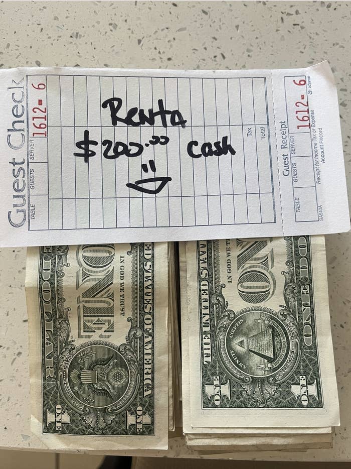 Guest check showing "Renta $200... cash" with a smiley face, placed above stacks of one-dollar bills