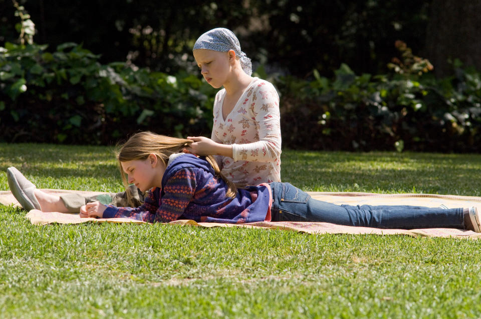 Abigail Breslin lies on grass reading, while Sofia Vassilieva, sitting behind her, braids Robb's hair in an outdoor park scene