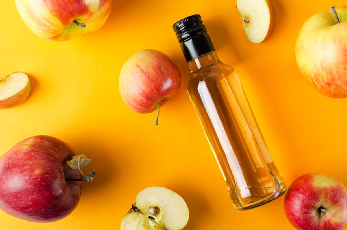 Bottle of apple cider vinegar surrounded by apples.