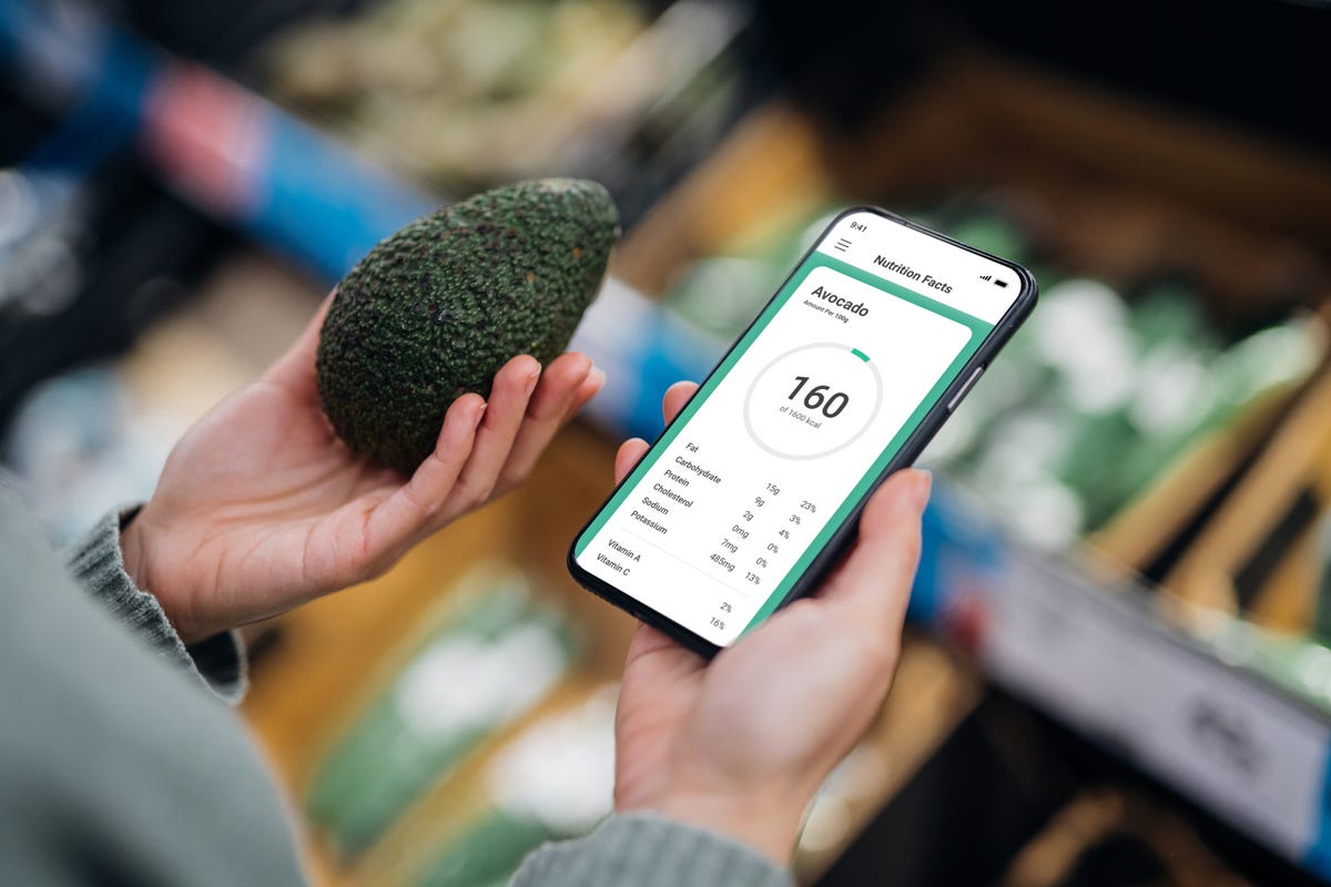 ver the shoulder shot of woman using mobile app to track nutrition and count calories of an avocado