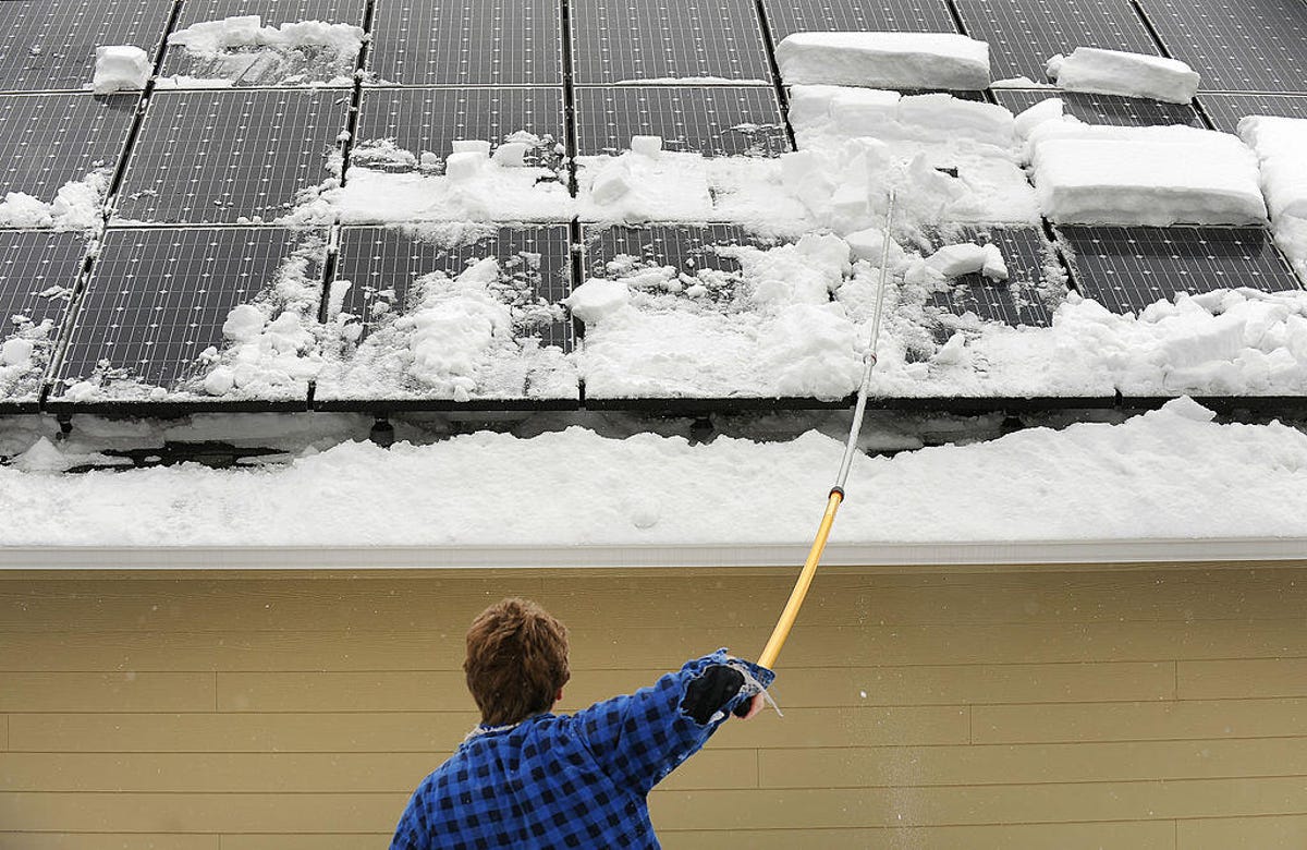 A person cleans snow off of solar panels.