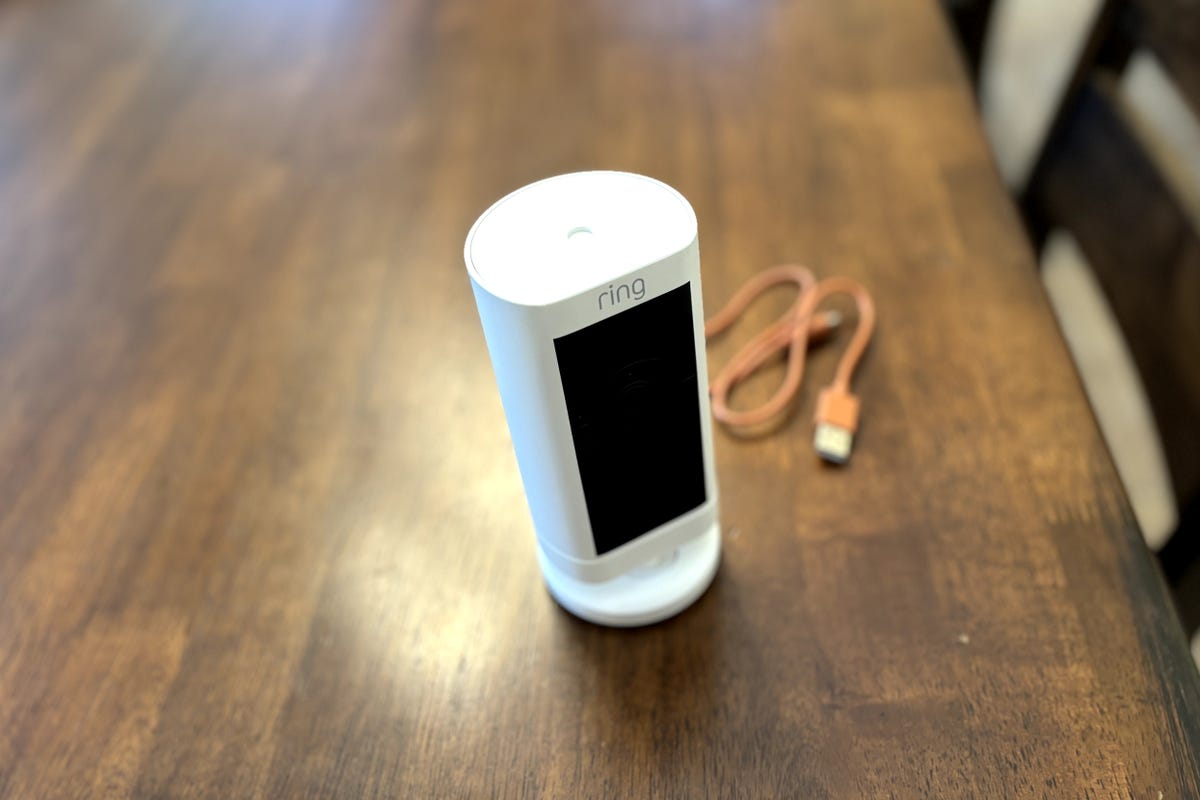 A Ring Stick Up Cam Pro on a wooden table with its charging table.