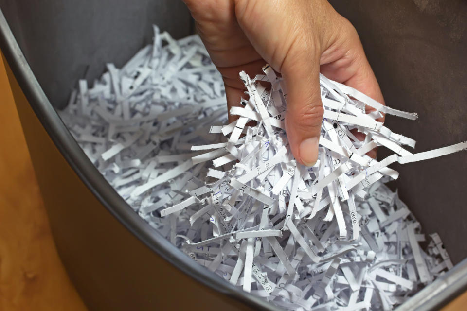 A hand is reaching into a bin filled with shredded paper