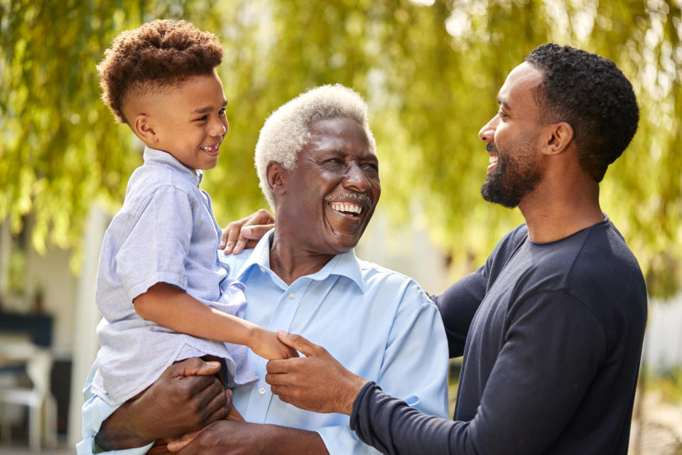 Three generations: A grandfather, father, and young boy share a joyful moment outdoors, smiling and laughing together