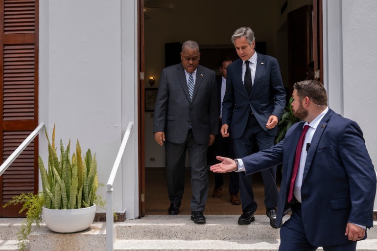 Garry Connille and Antony Blinken leave a US diplomatic facility in Port-au-Prince. An aide guides their way, gesturing down the steps.