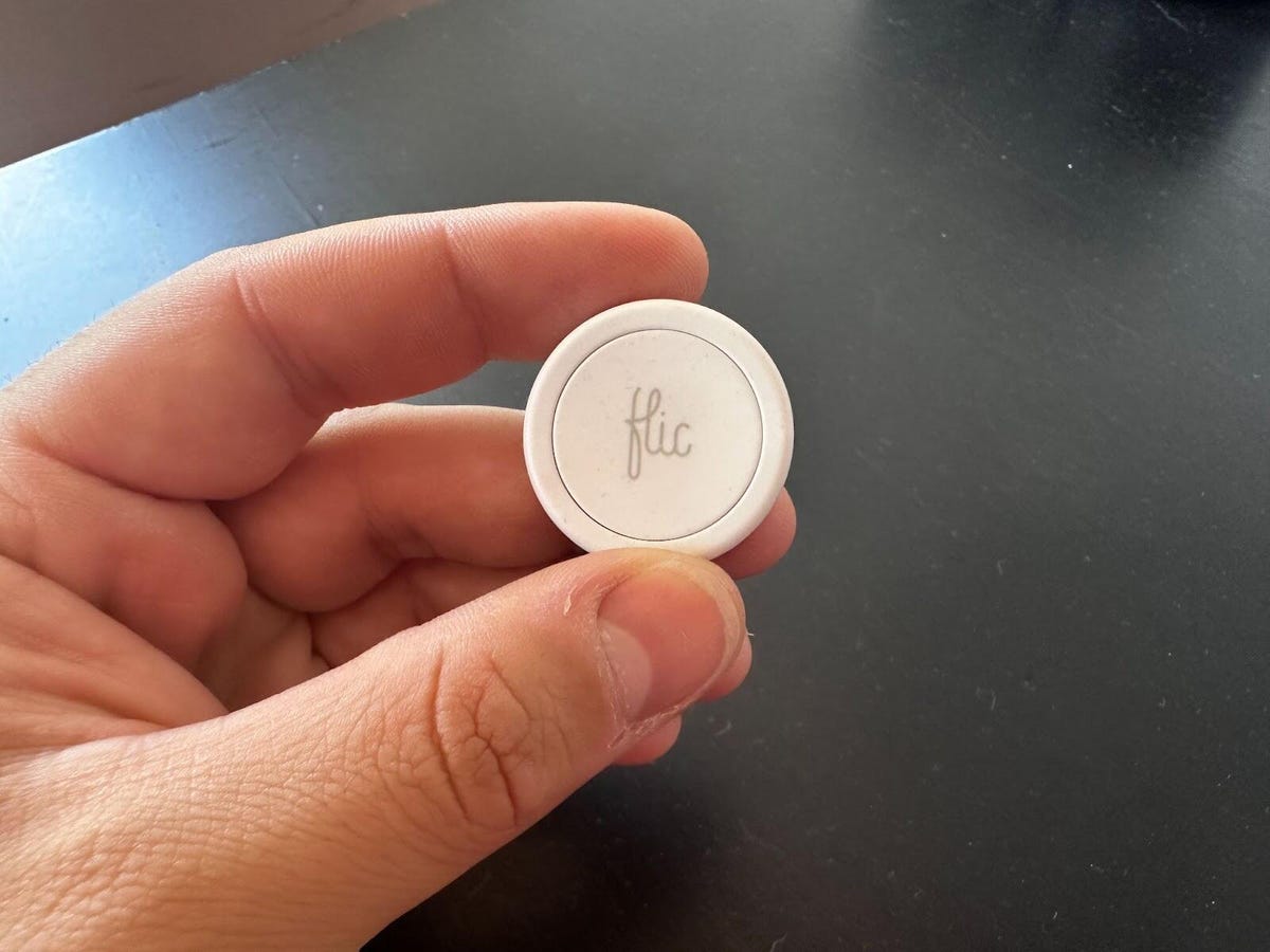 hand holding a Flic button in front of a table
