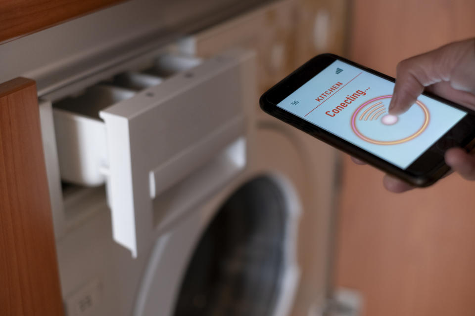 A hand holding a smartphone with a "Connecting..." message displayed, near an open washing machine detergent tray