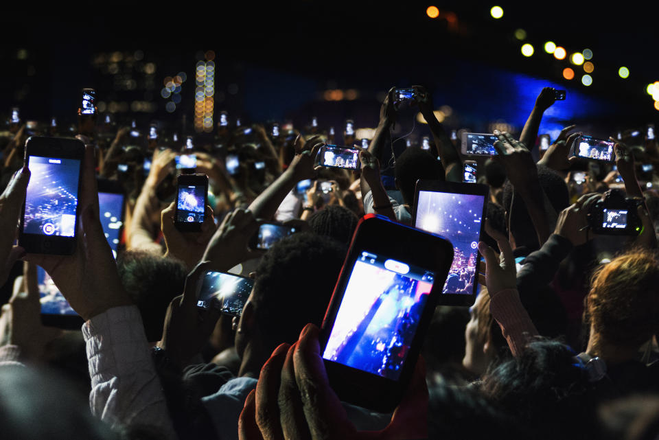 Crowd of people at a concert holding up smartphones, capturing video and photos of the event