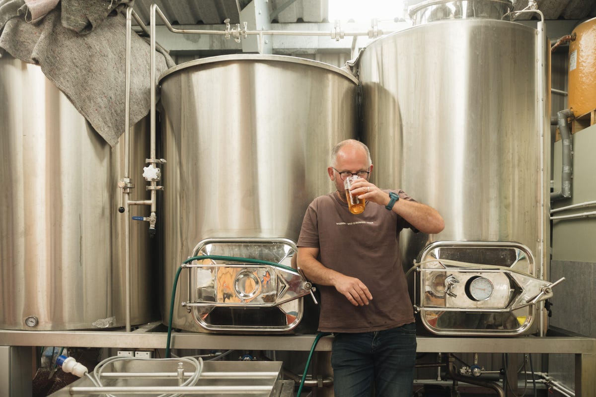 Man drinking a beer with stainless steel tanks behind him.