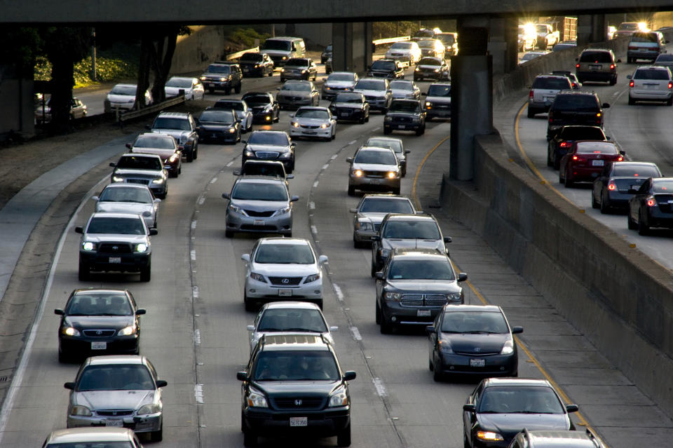 A busy freeway filled with cars. Dense traffic moves slowly in both directions under an overpass