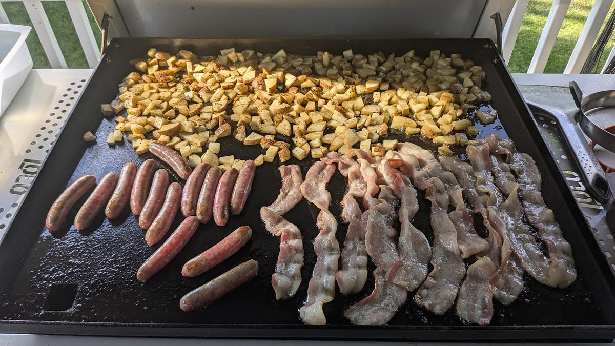 Sausage, potatoes, and bacon cooking on a griddle.