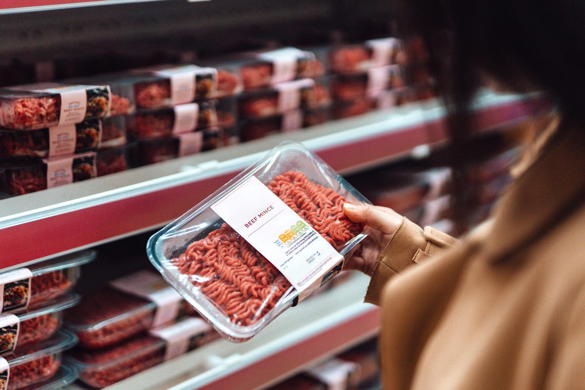 Above the shoulder view of woman holding a pack of beef mince in a supermarket.