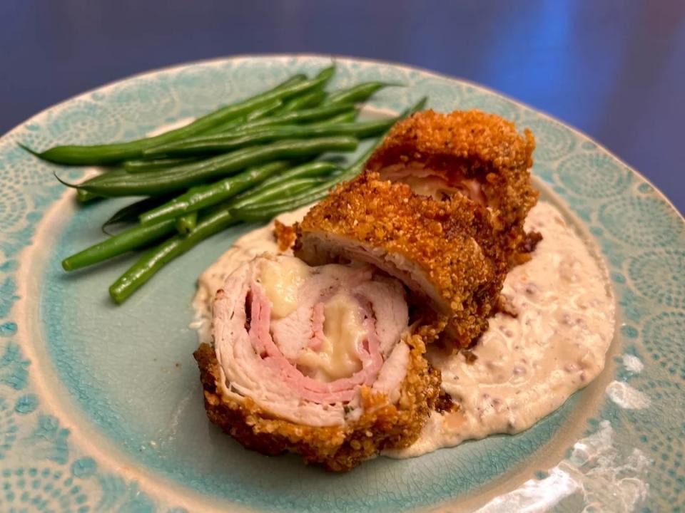 Breaded chicken cutlet stuffed with ham and cheese, served with green beans, on a decorative plate