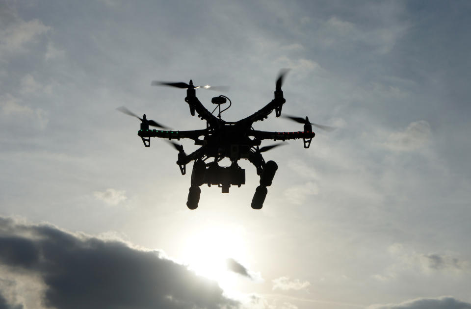 A drone with multiple rotors is flying in the sky with the sun shining behind it, silhouetting its structure