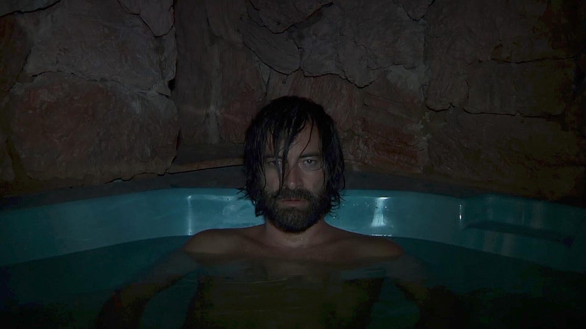 a scene from the movie Creep 2, showing Mark Duplass as Aaron sitting alone in a bathtub, looking a bit downtrodden and very serious