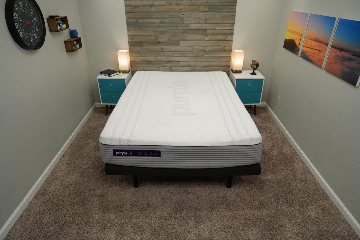 The Purple mattress in a bedroom with a wooden backdrop and beside two nightstands.