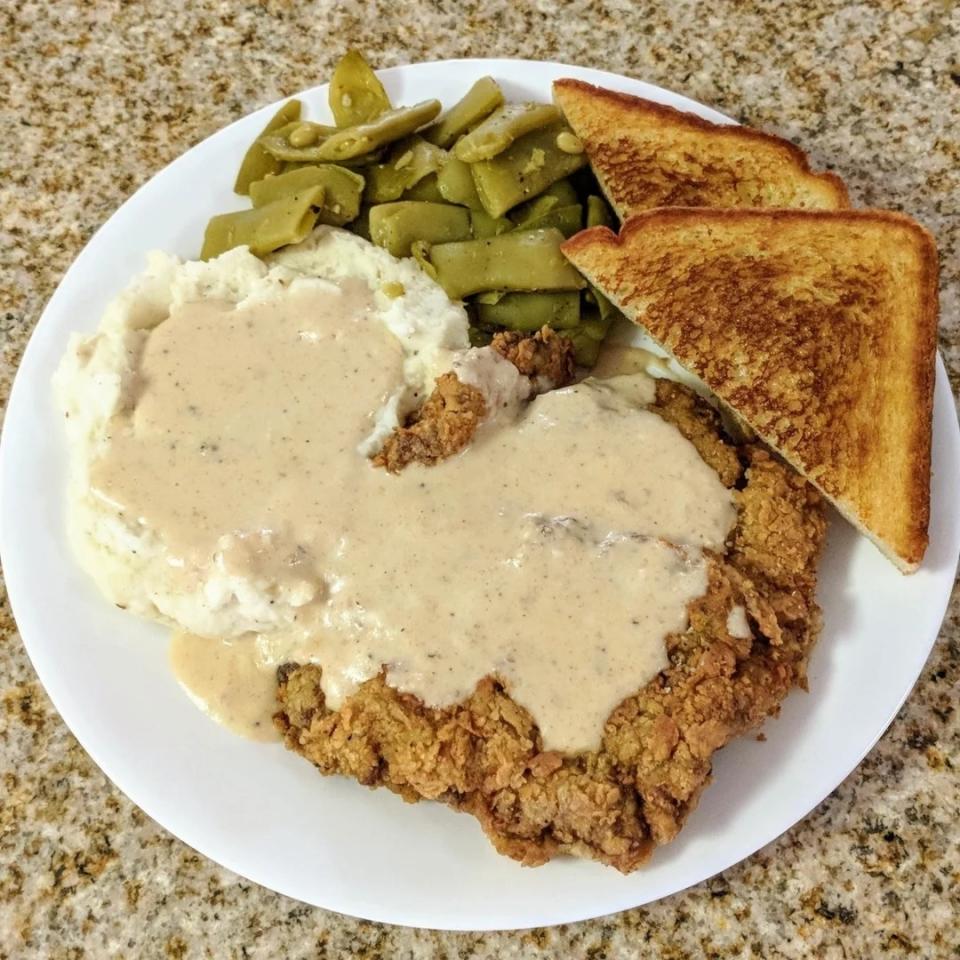 Plate with chicken-fried steak and gravy, mashed potatoes, green beans, and two slices of toast