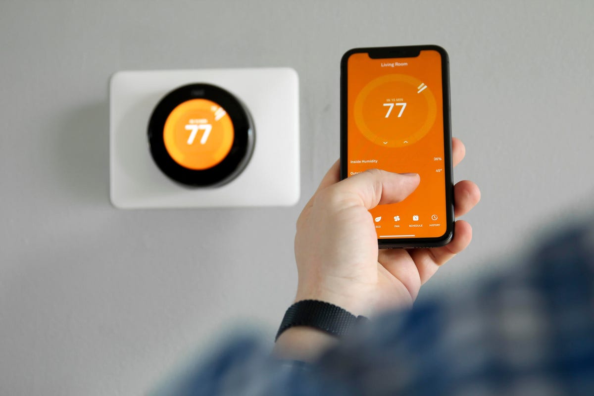 A person holds a phone in front of a smart thermostat.