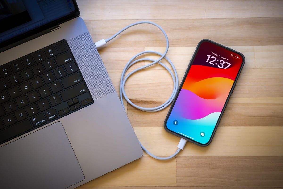 iPhone connected to a MacBook Pro laptop via a sync cable.