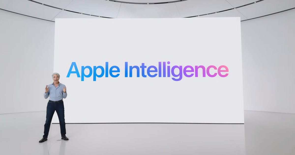 apple intelligence text on screen, with a man standing in front of the screen wearing a blue button down top and black slacks.