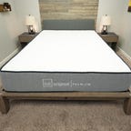 A gray and white Lull Original Premium mattress on a wooden bed frame in a gray-carpeted bedroom.
