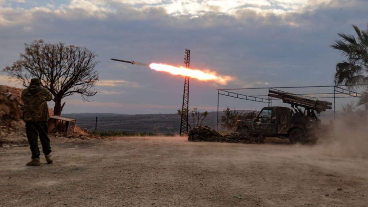 An anti-government fighter covers his ears as a multi-barrel rocket launcher fires against regime forces in the northern outskirts of Syria's west-central city of Hama on December 4, 2024. Syrian government forces pressed a counterattack against Islamist-led rebels around the key city of Hama on December 4 after suffering a string of staggering losses further north, a war monitor said.