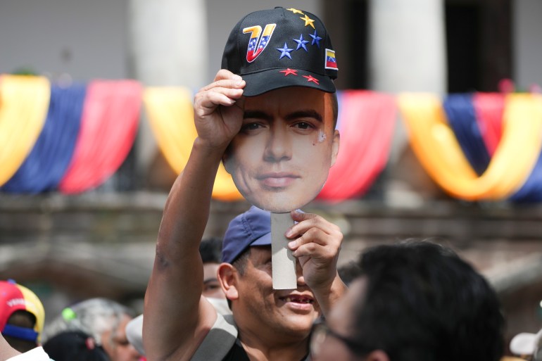 A supporter holds up a cut-out of Daniel Noboa's head and holds a baseball cap over it.