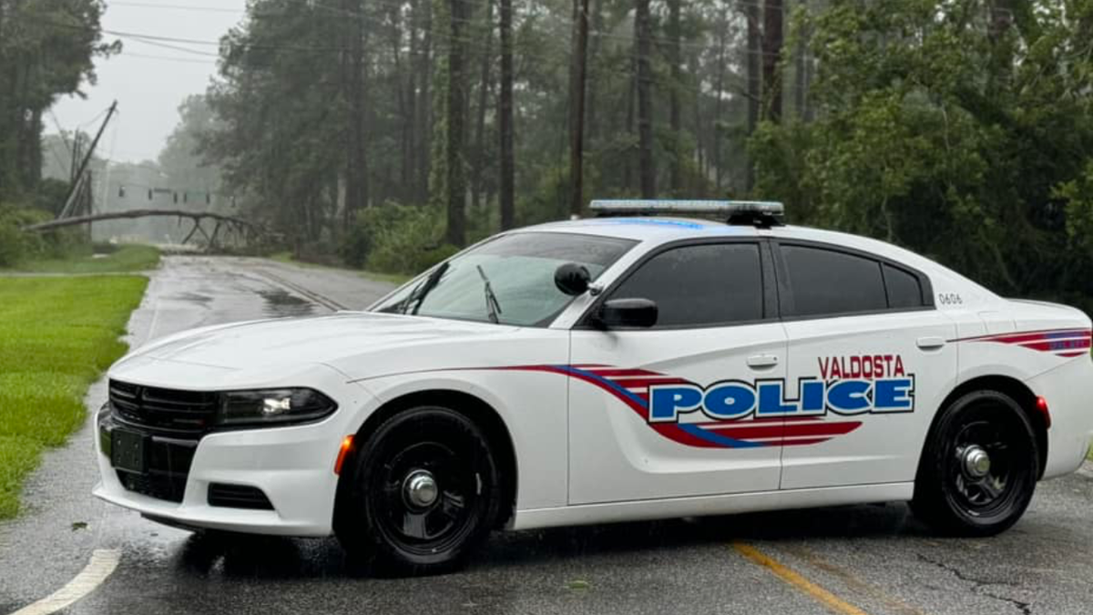 A Valdosta, GA, police vehicle can be seen blocking a road with a tree down.