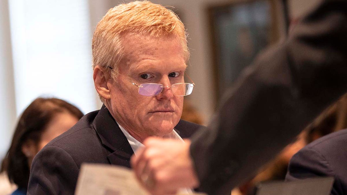 A man wearing glasses looks on while in a courtroom.