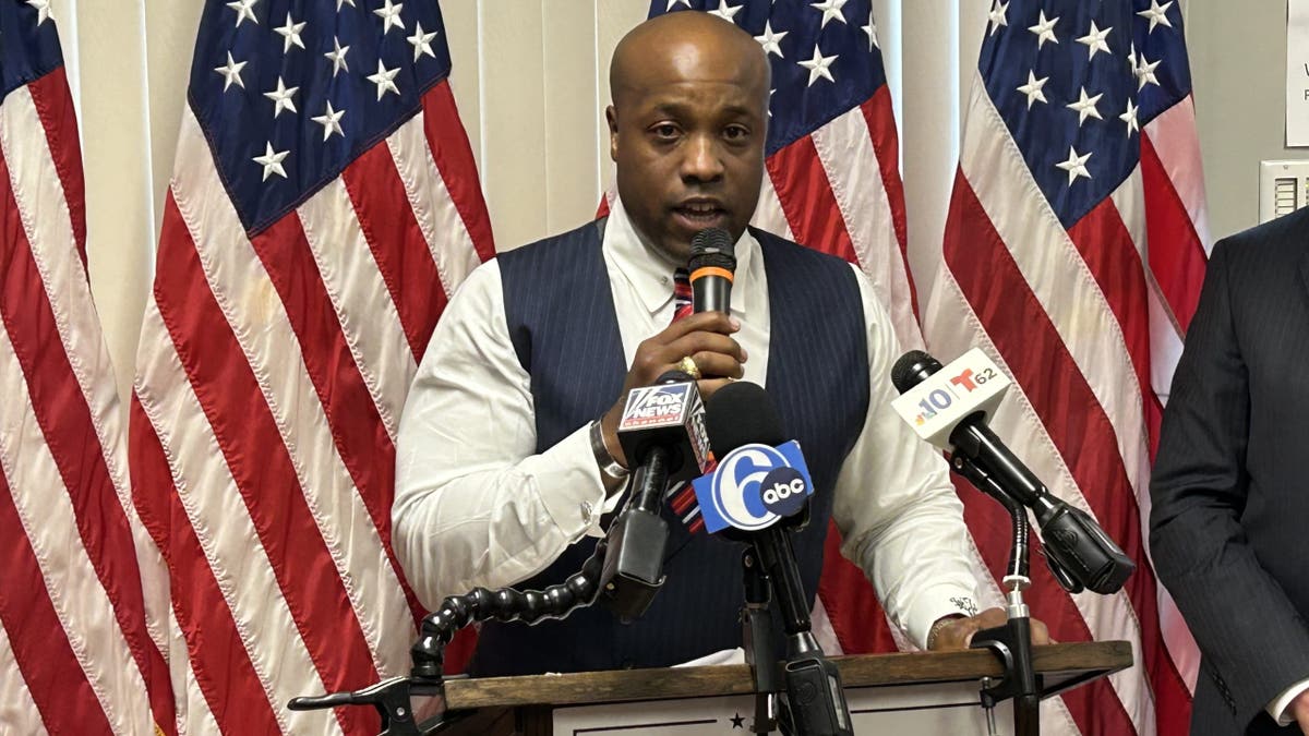 Wesley Hunt holding microphone at lectern, US flags behind him