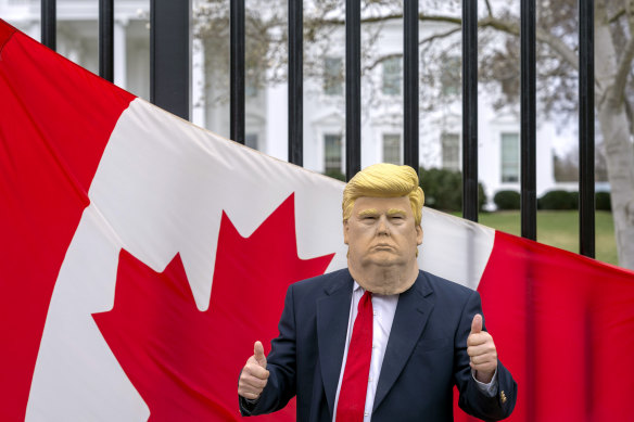 A visitor to Washington wears a Donald Trump mask in front of a Canadian flag in outside the White House.