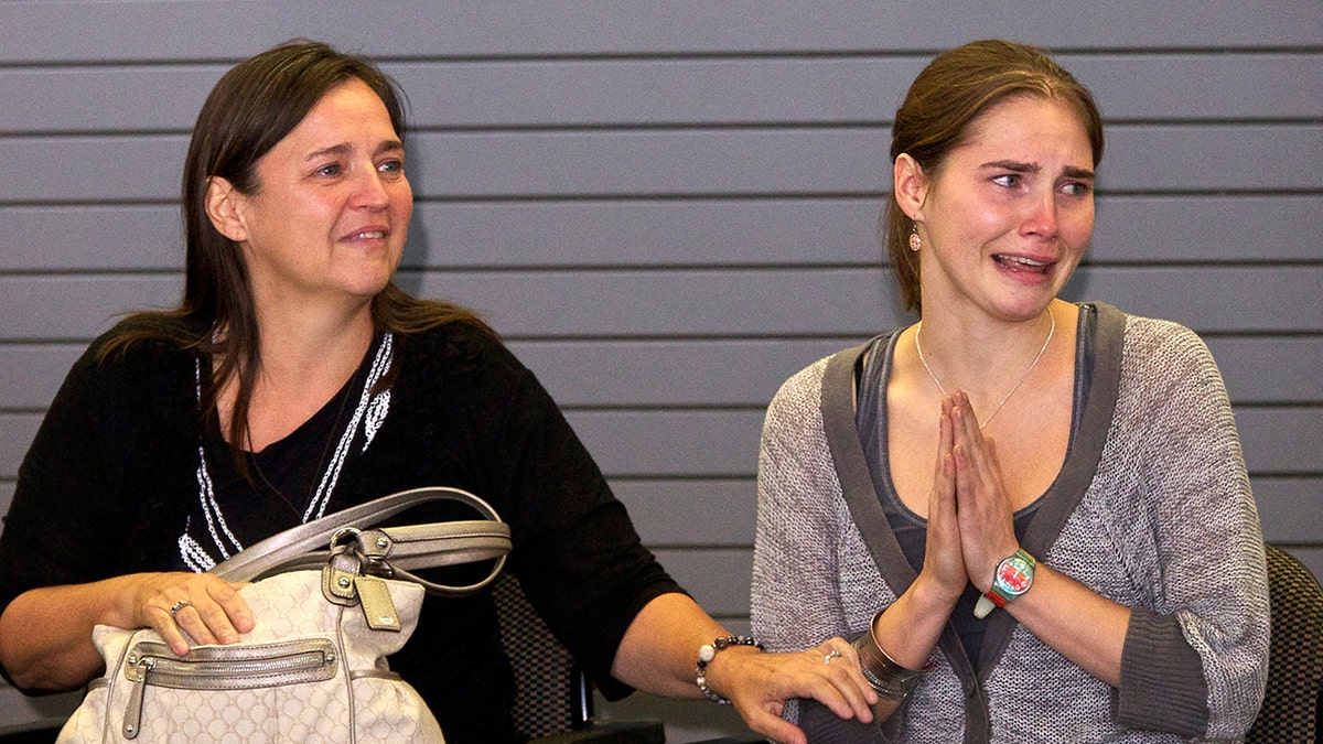 Amanda Knox crying with her hands in a prayer stance sitting next to her mother.