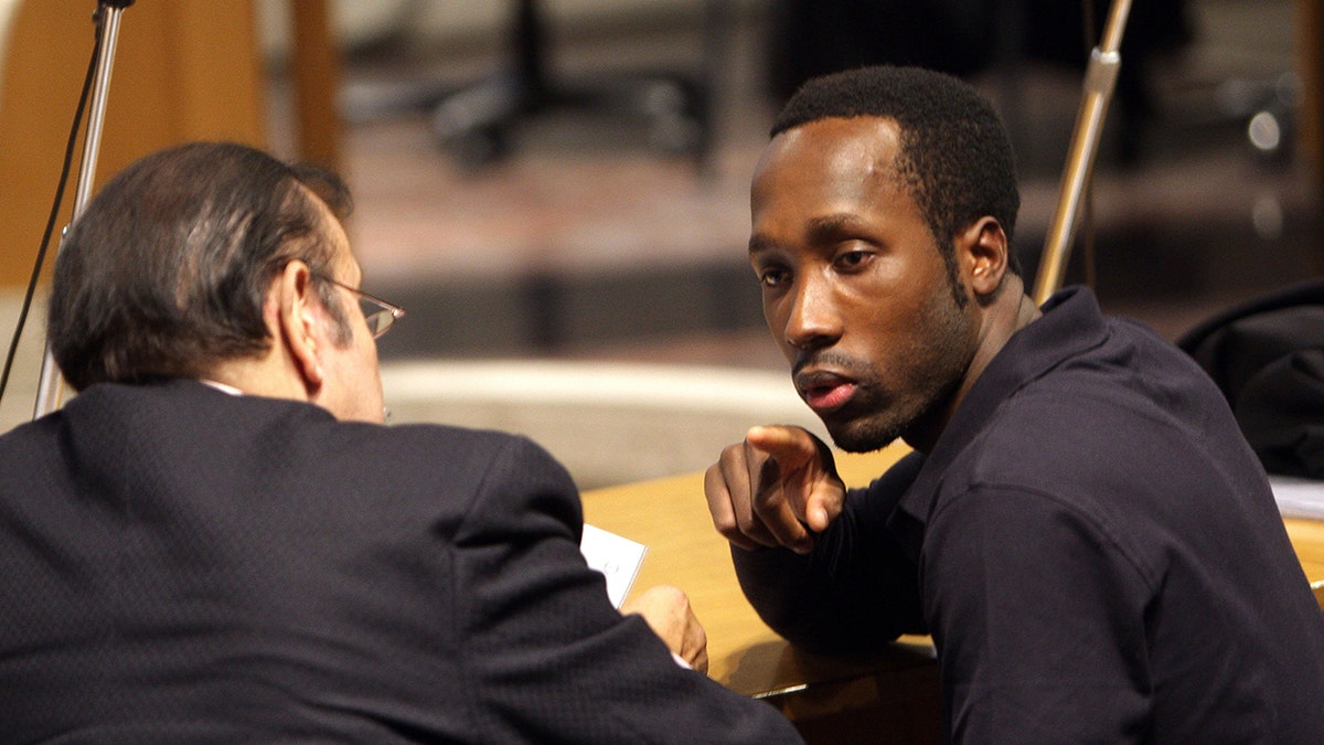 Rudy Guede sitting in a court room wearing black.