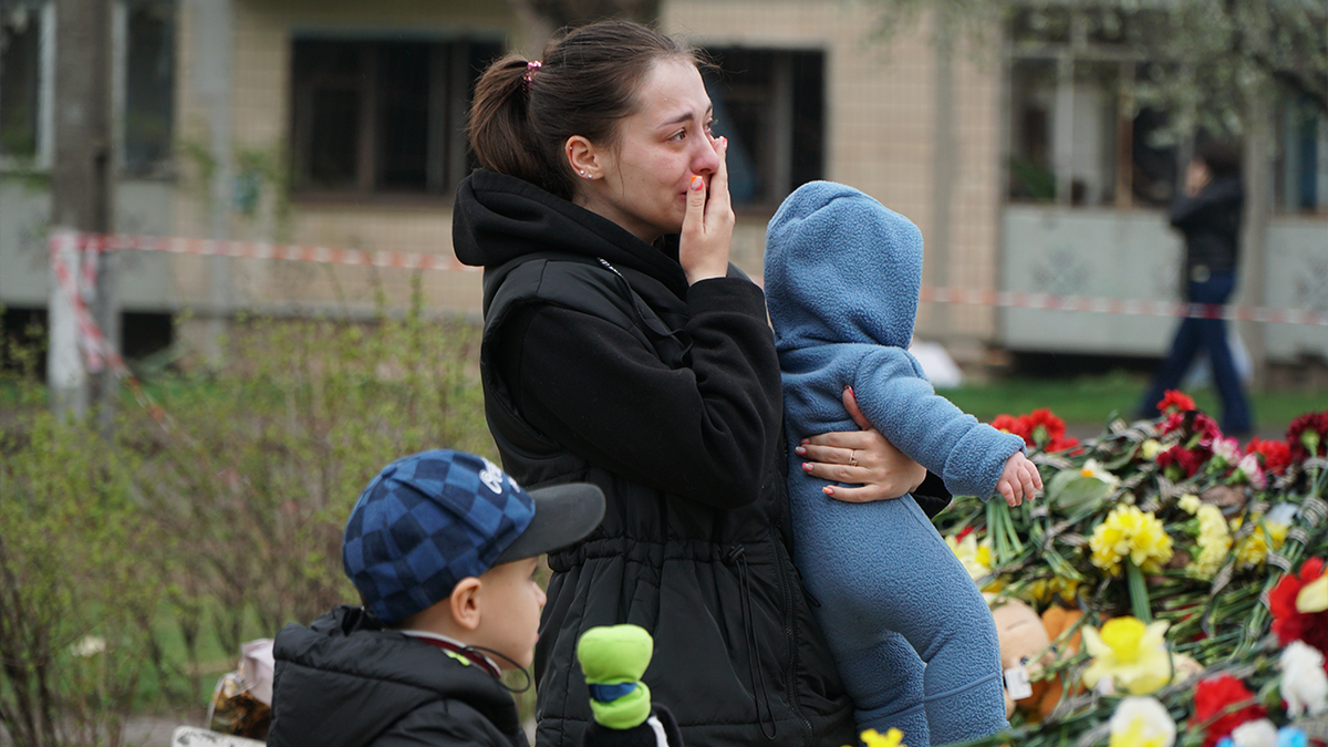 A woman with her children mourns near a memorial for war victims. 