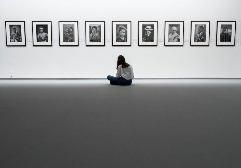 A visitor sits in front of a series of photos on an exhibit wall.