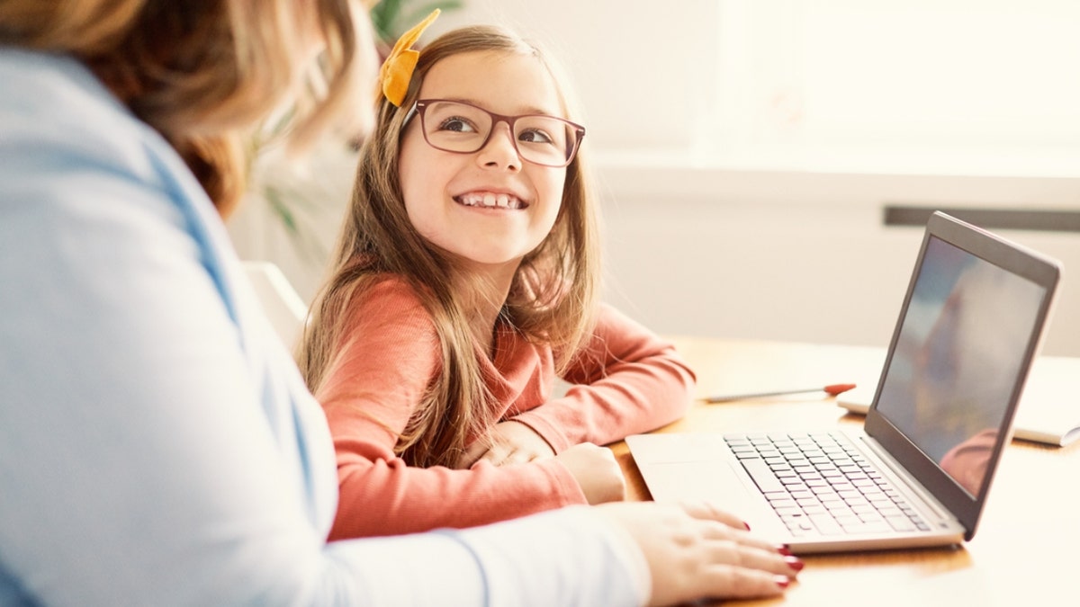 a little girl smiles at parent in front of laptop
