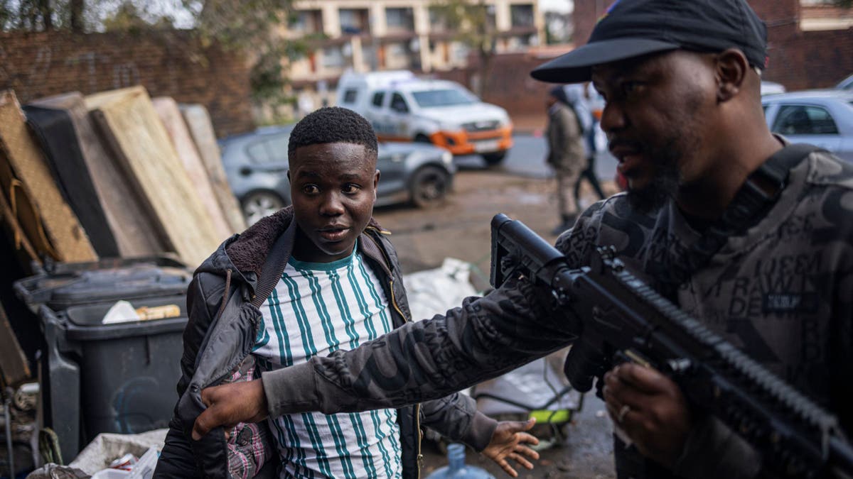A plainclothes police officer with the Johannesburg Metro Police Department questions a man found inside a dilapidated building used as a shelter in Johannesburg on May 15, 2023.