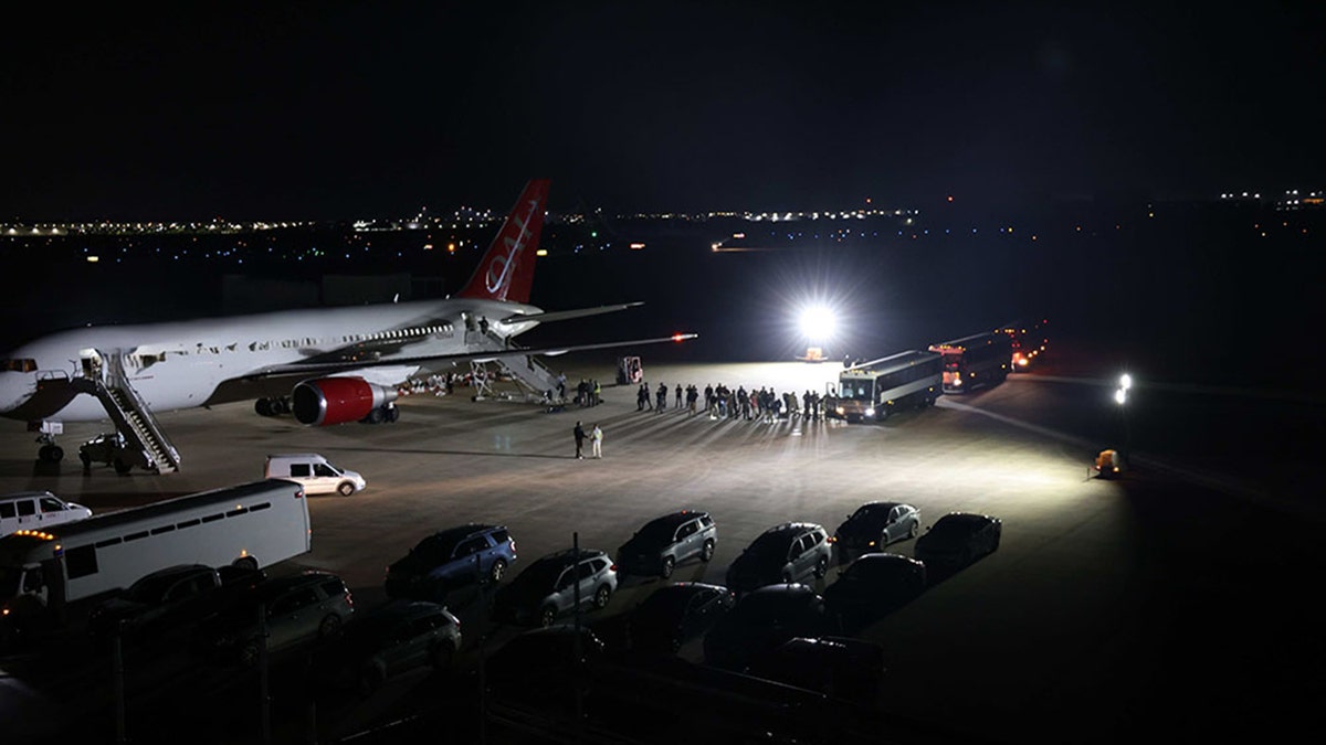Nighttime view of an ICE deportation operation with a large passenger plane and ICE vehicles