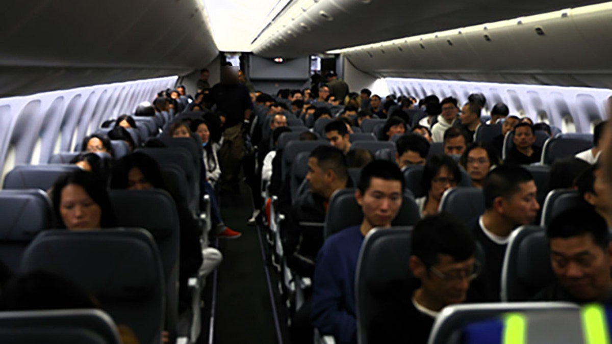 Interior view of an airplane cabin filled with seated deportees awaiting departure