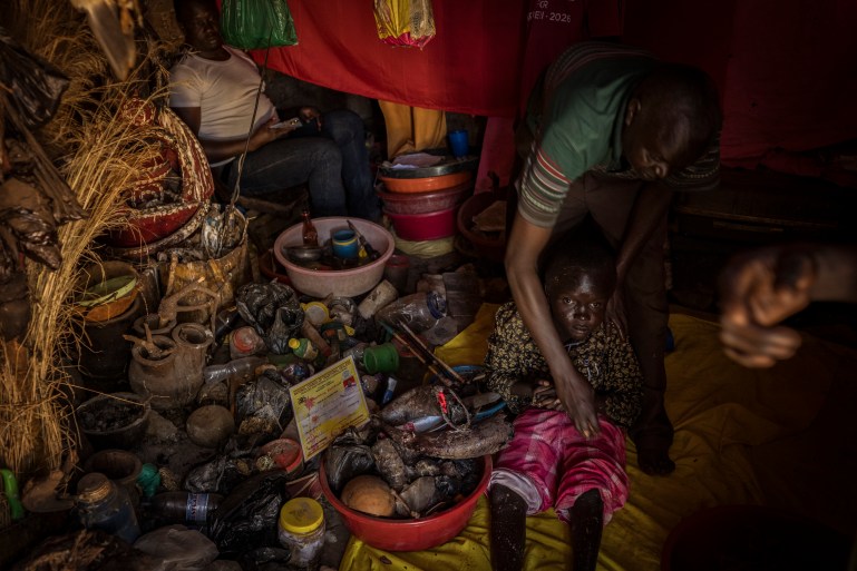 Omalera, Soroti District, Uganda. Local Witch doctor Robert Apedu treats Noah Oyara,17. Noah has no use of his legs and also lives with hydrocephalus. Robert treated these conditions by rubbing a paste of water and plant matter into Noahs skin. While he is well known in the area as a witch doctor, he understands the negative connotation surrounding his profession so like many others he refers to himself as a 'traditional healer or herbalist'. [Christopher Hopkins/Al Jazeera]