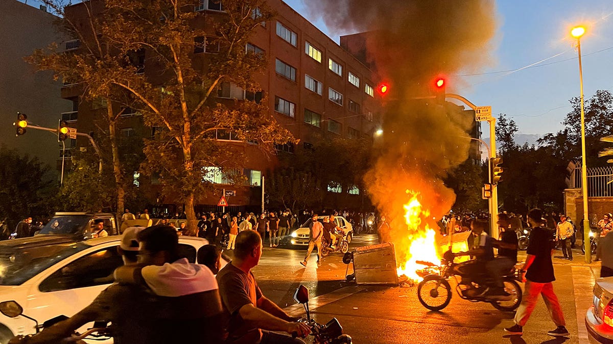 A fire releases a large amount of smoke with protesters gathered around it