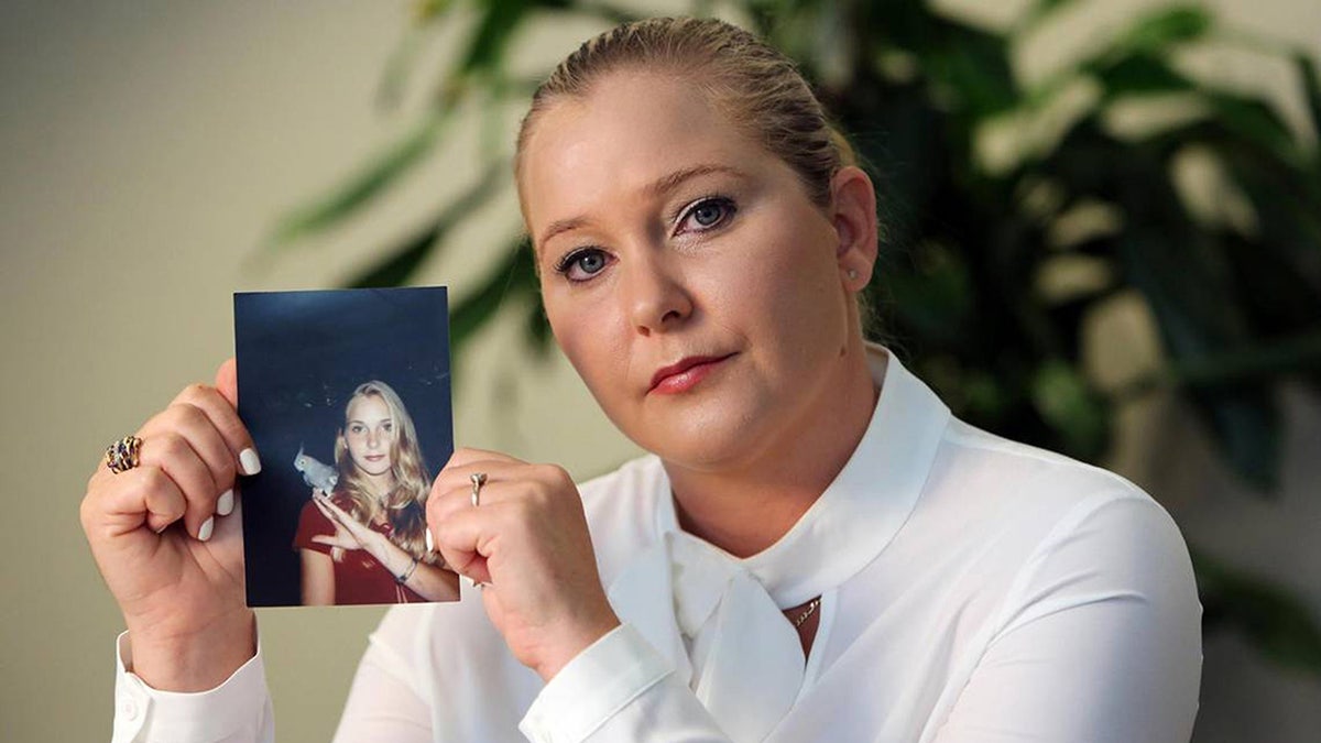 Virginia Guiffre holding a photo of herself swearing a white turtleneck.