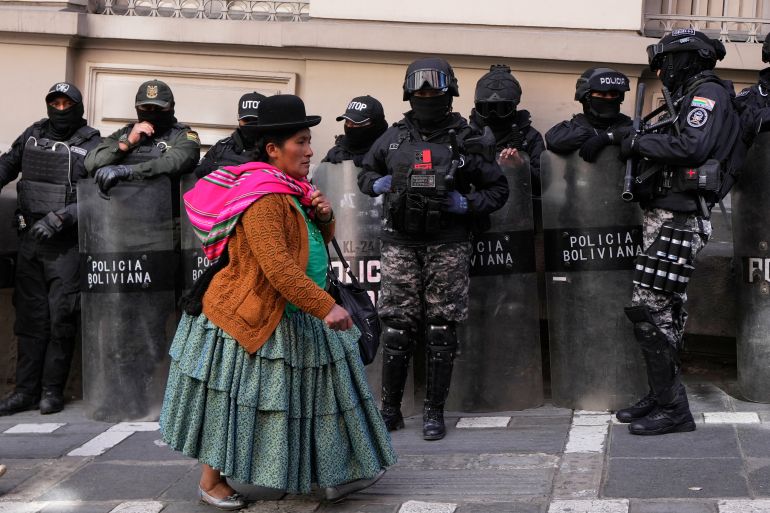An Indigenous woman in Bolivia walks past police in riot gear