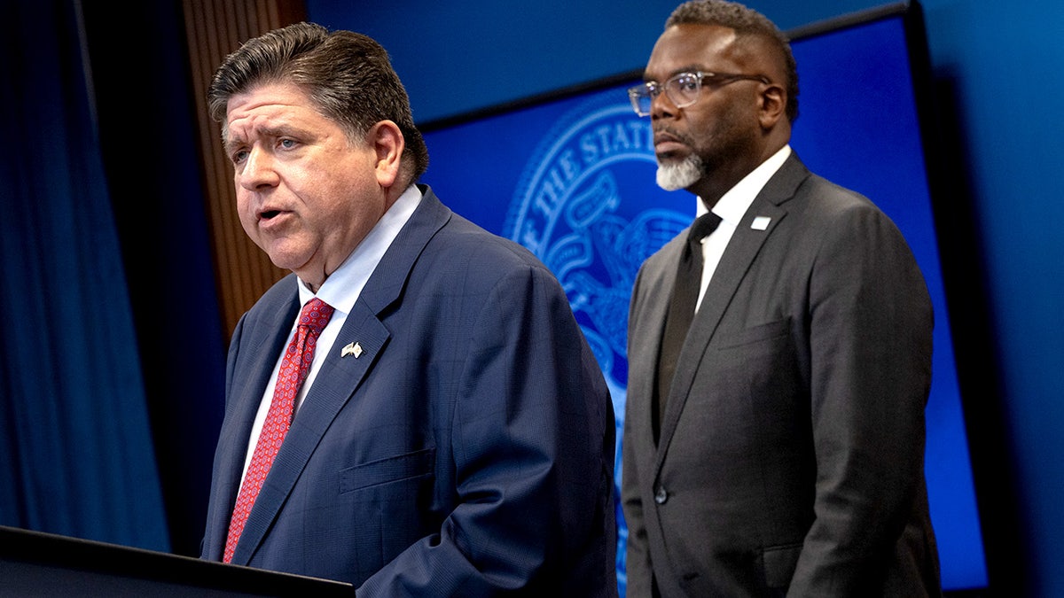 Illinois Governor JB Pritzker speaking at a press conference while Chicago Mayor Brandon Johnson listens