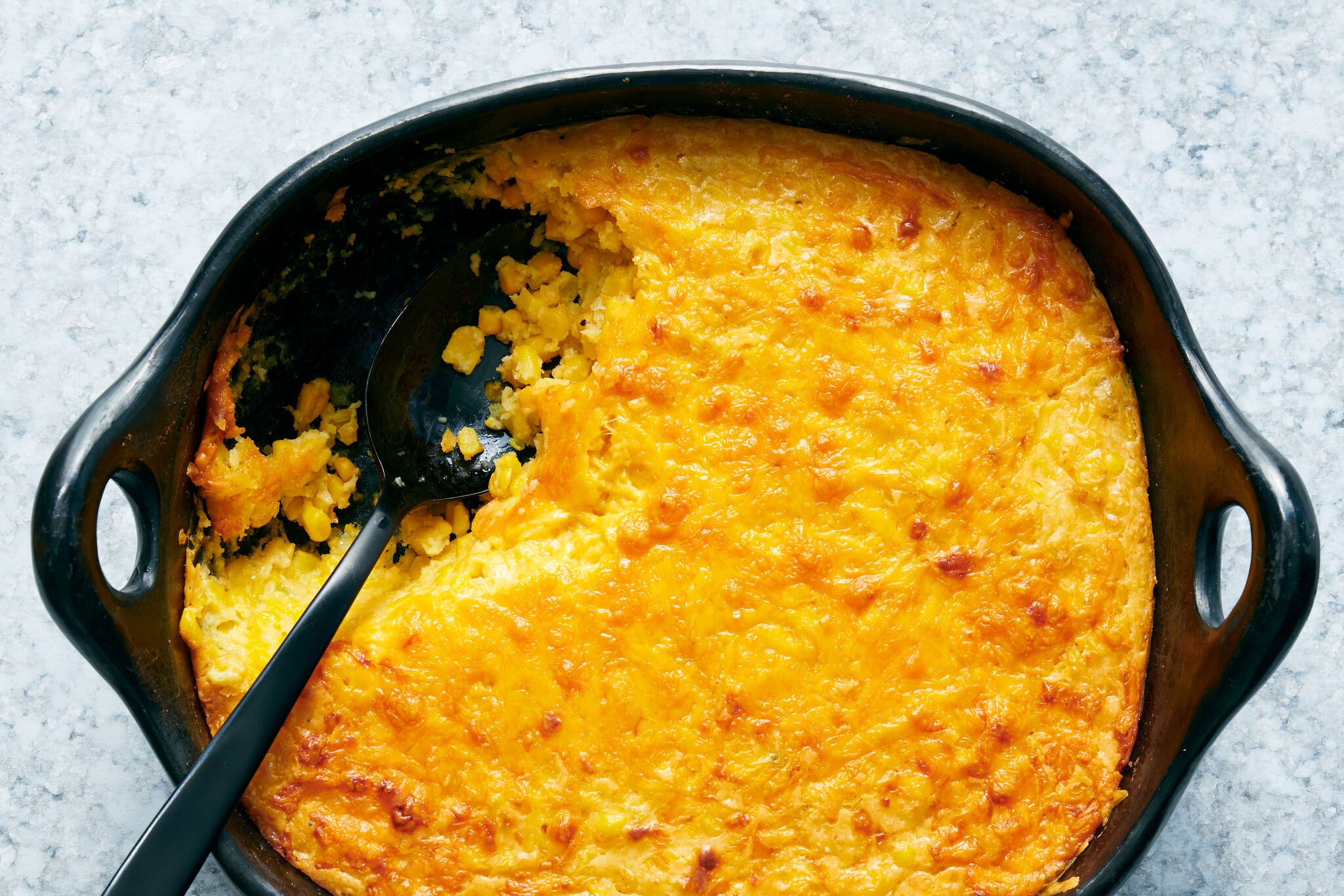 An overhead image of a baking dish filled with corn casserole. A spoon sits where a serving is removed.