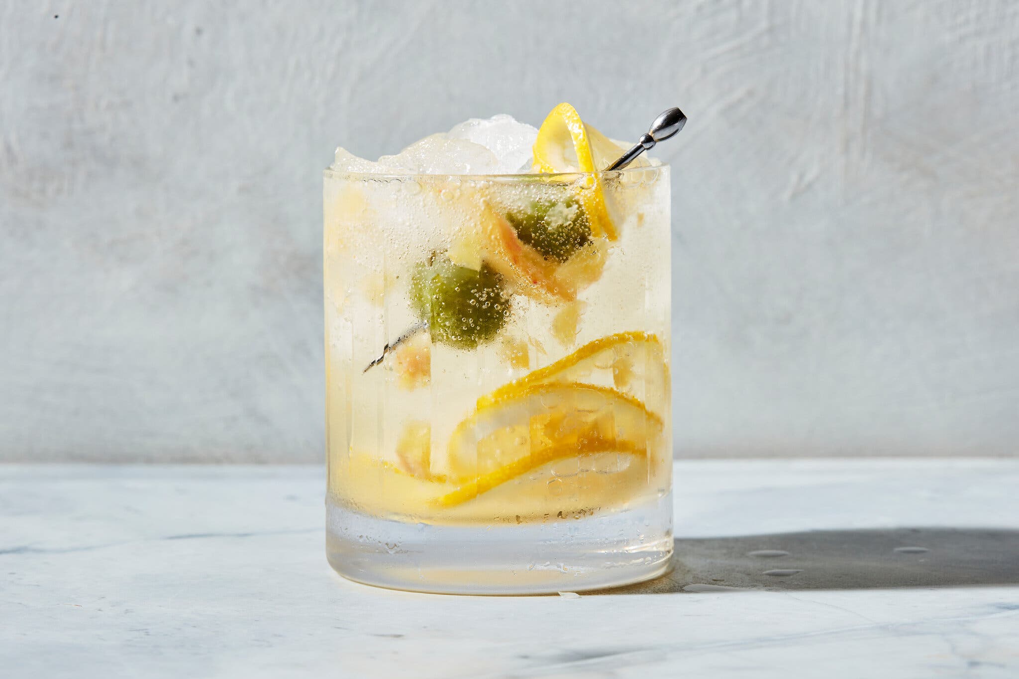 A rocks glass of tonic, with a skewer with two olives and a lemon twist