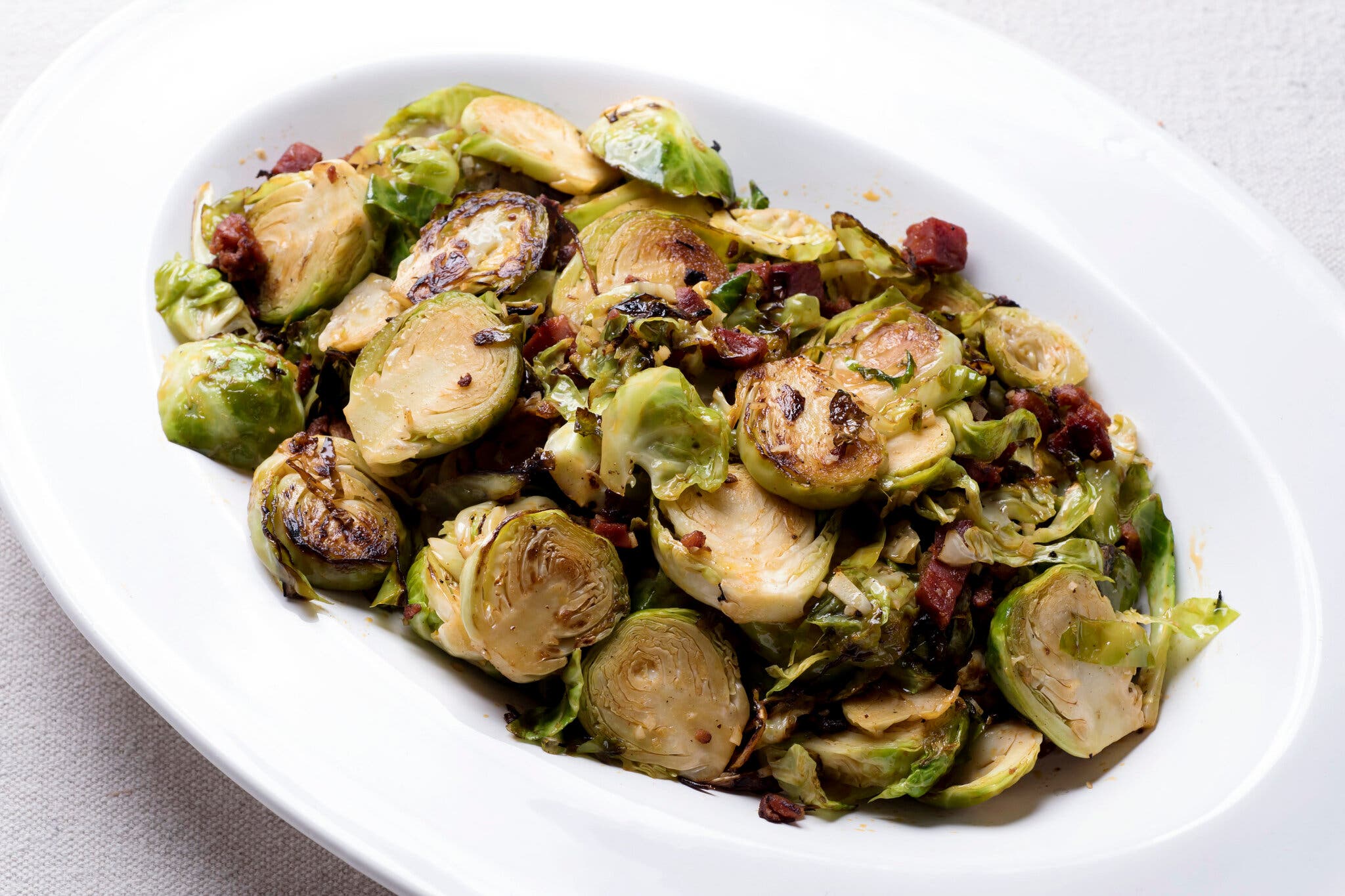A platter of brussels sprouts and chorizo, photographed from the side.